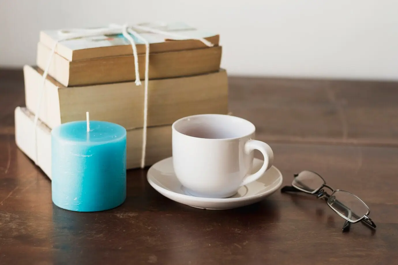 Ein Bücherstapel, eine blaue Kerze, Kaffee und eine Brille auf einem Tisch.